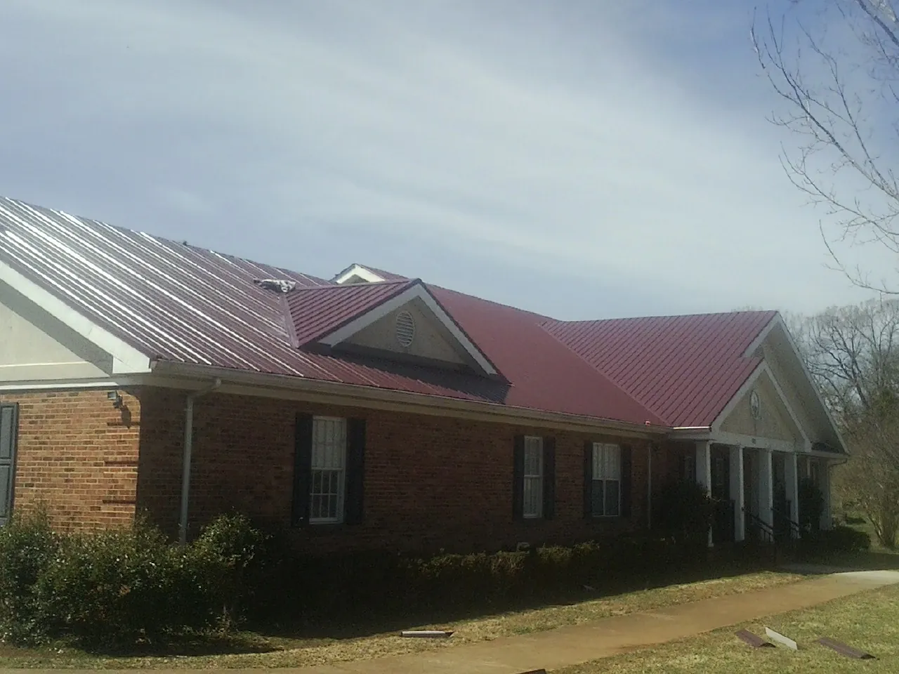 Red metal roof with gabled entries on a long brick building, from a Hail Damage Roof Repair job in Rosebud